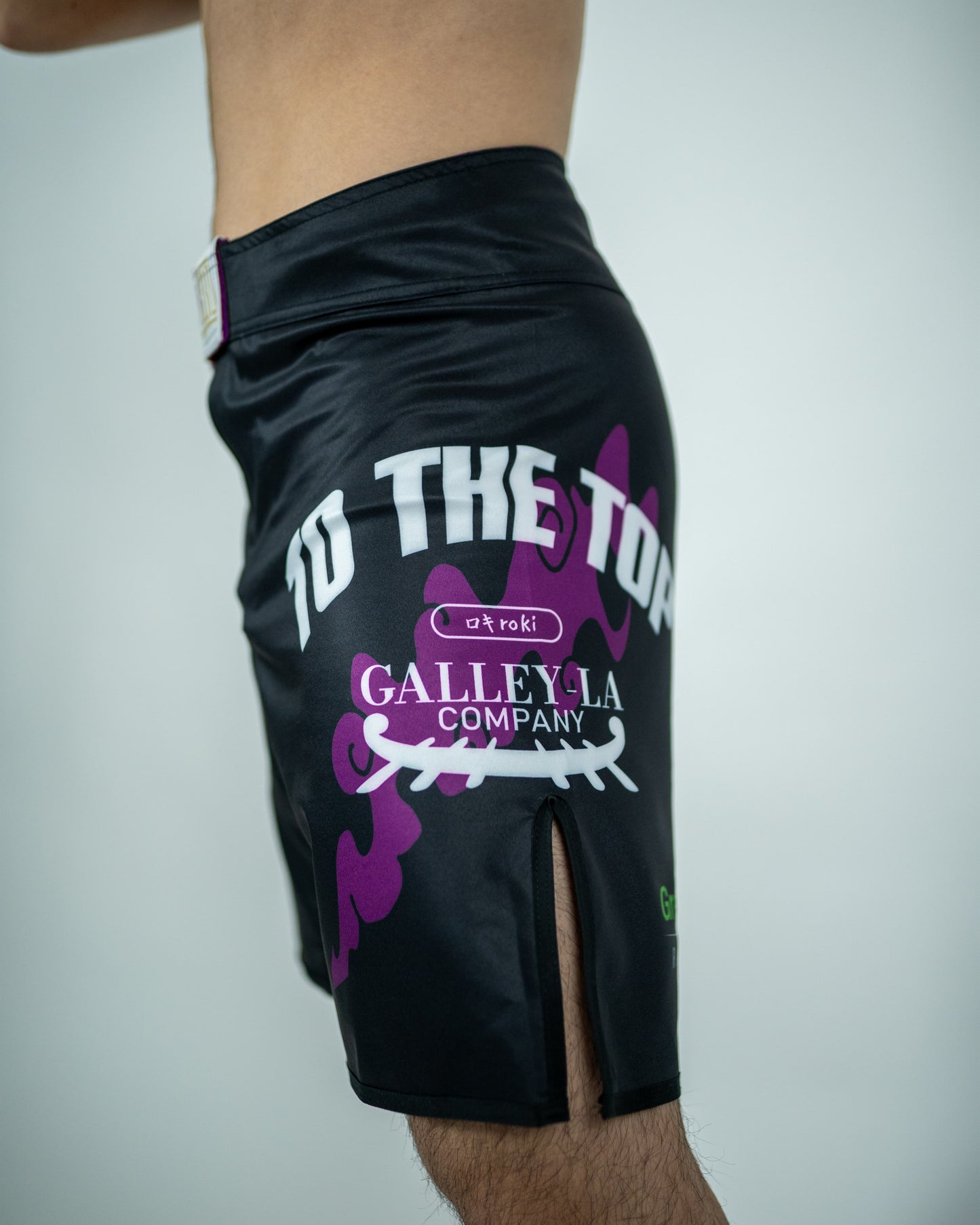 Side view of a model wearing Roki grand line fight shorts, featuring purple accents, Roki logo, and manga-inspired sponsor logos