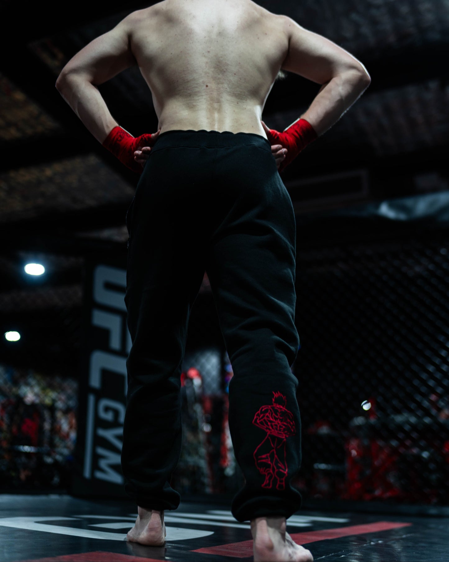 Fighter standing barefoot in UFC cage wearing Grappler Joggers with red demon back embroidery on lower leg
