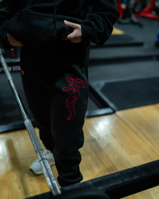Grappler Joggers worn in gym with red demon back embroidery visible during barbell setup on platform