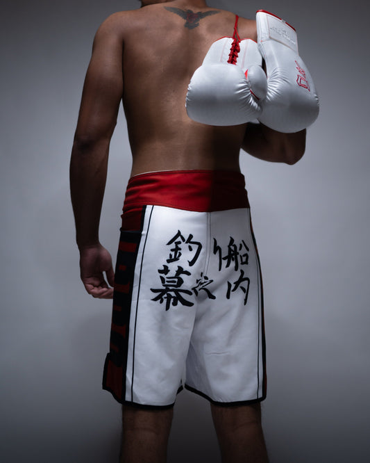 Back view of Ippo Fight Shorts featuring Japanese kanji and red waistband, worn by model holding boxing gloves