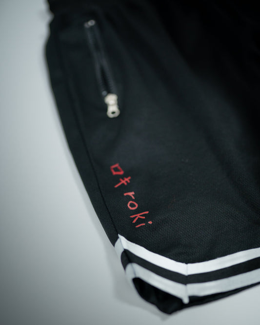 Close-up of Roki Gym Shorts showing red logo print, zip pocket, and white striped hem detai