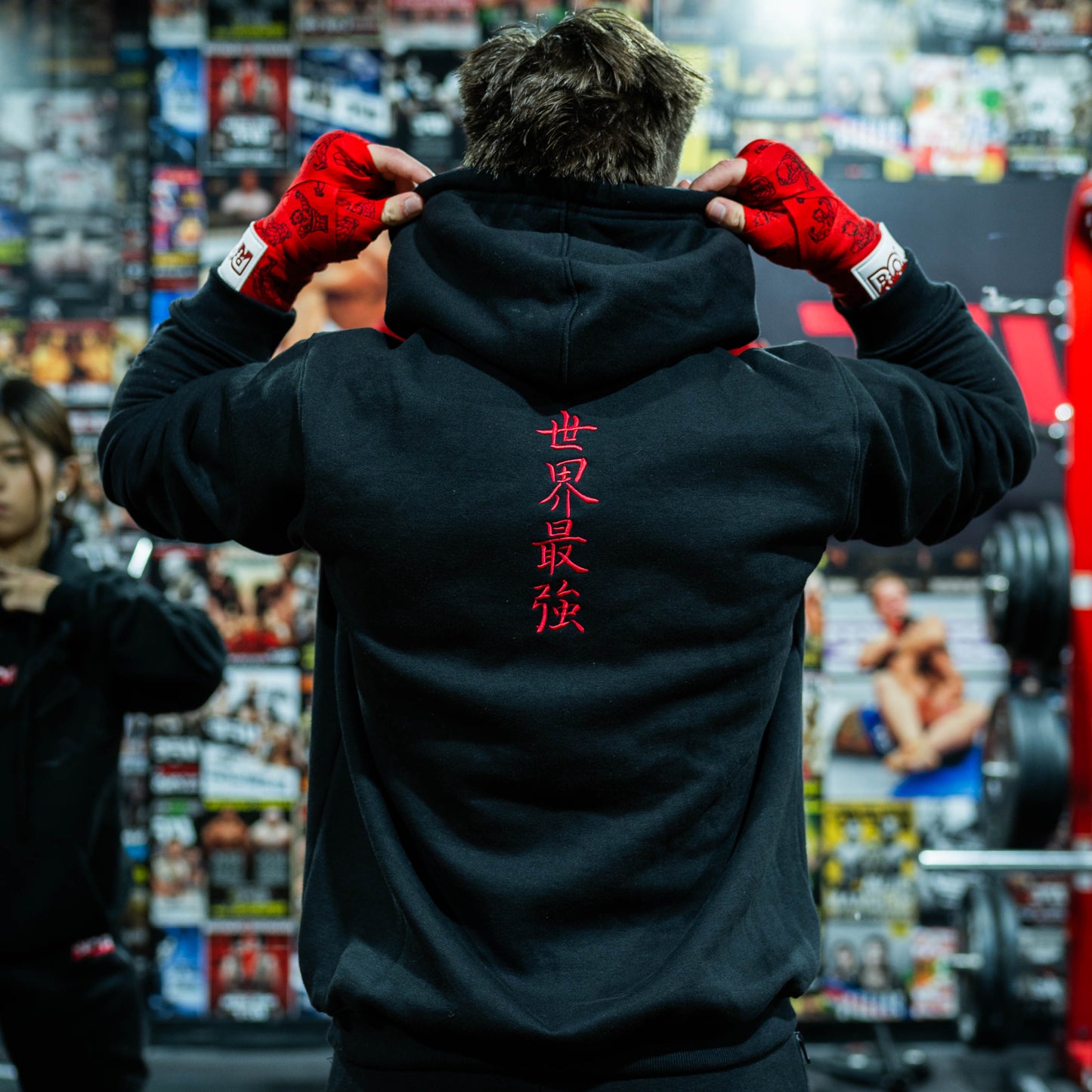 Model wearing Sekai Saikyo Hoodie in gym showing red Japanese kanji on back inspired by Baki Hanma