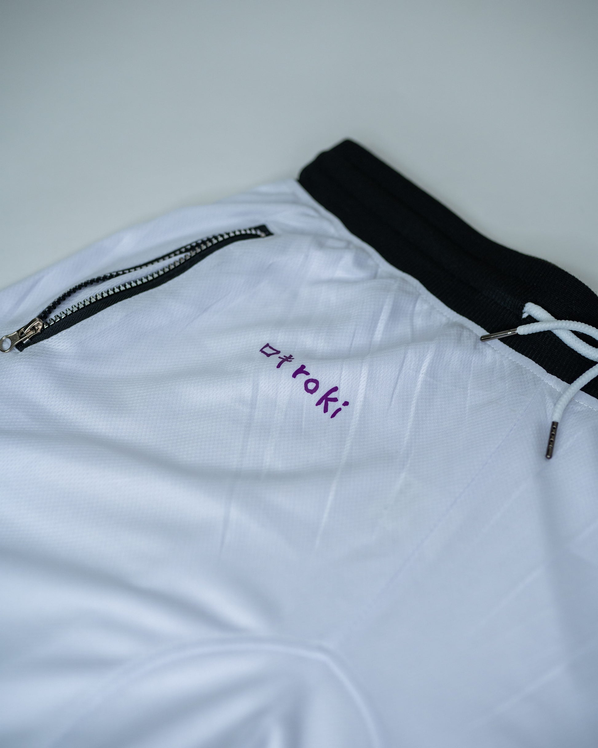 Close-up of white Roki Awakened gym shorts featuring purple accents and Roki logo