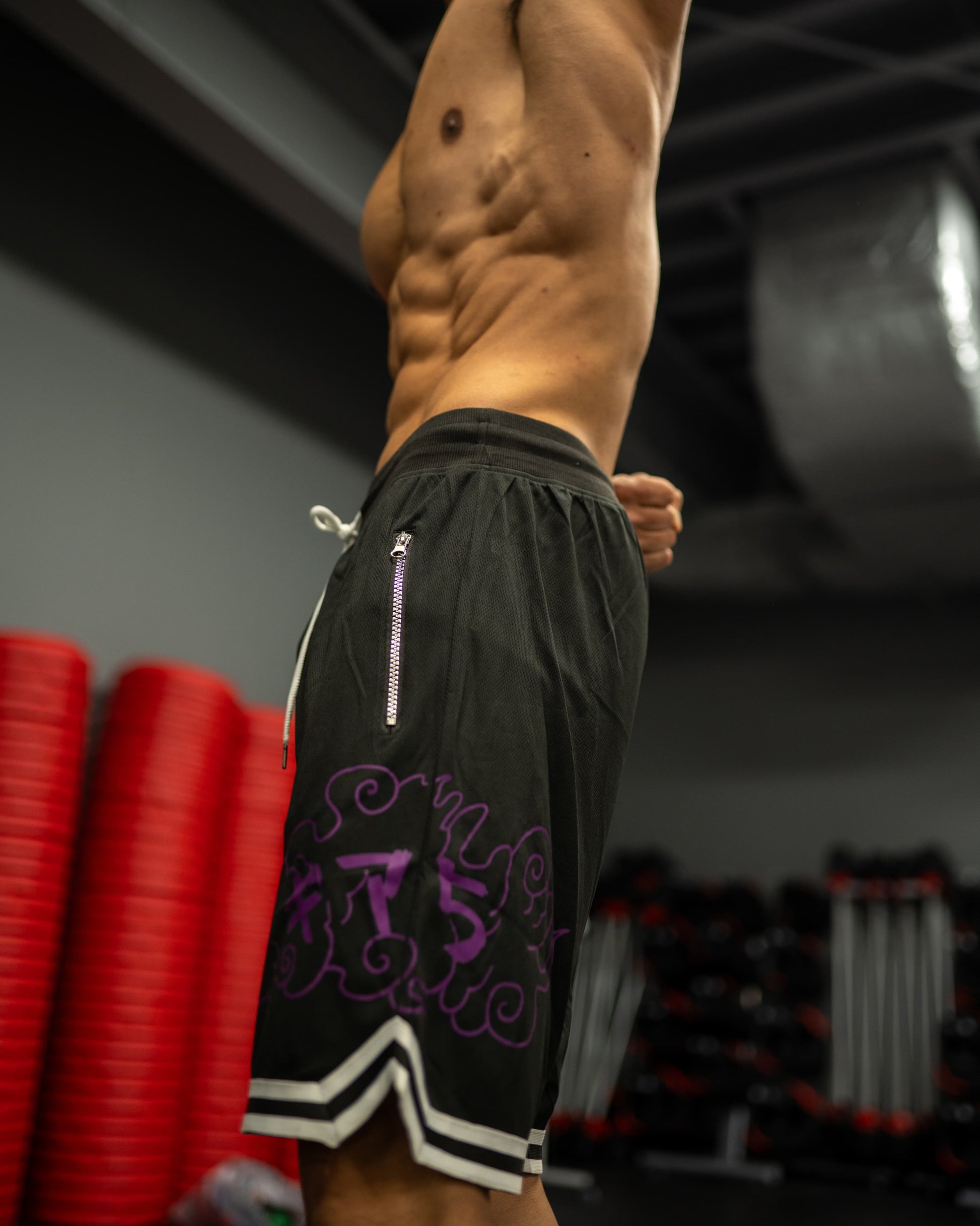 Side view of shredded model wearing black Roki awakened gym shorts