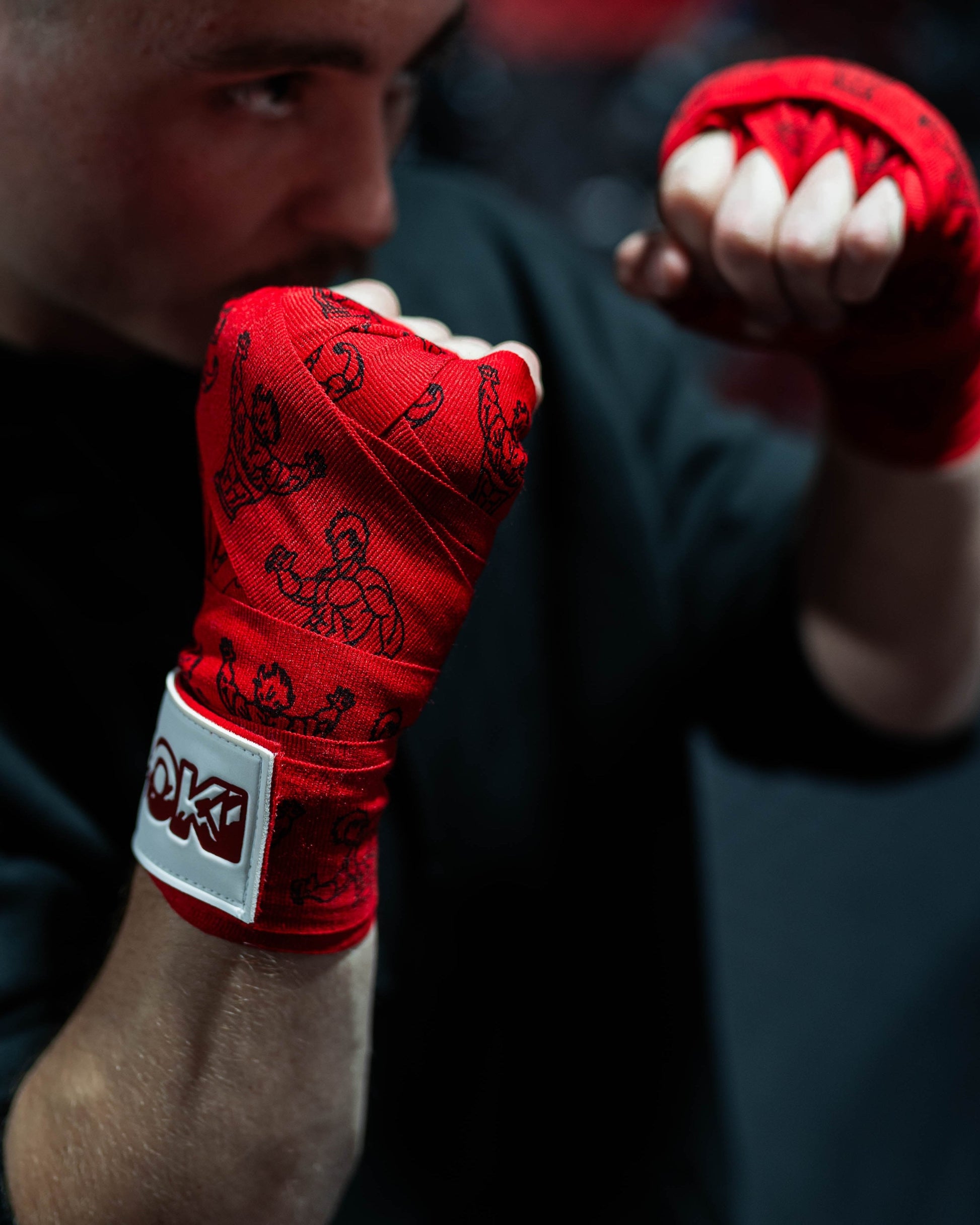 fighter wearing red anime-inspired boxing hand wraps in combat stance, grappler pose design visible with roki logo patch on wrist