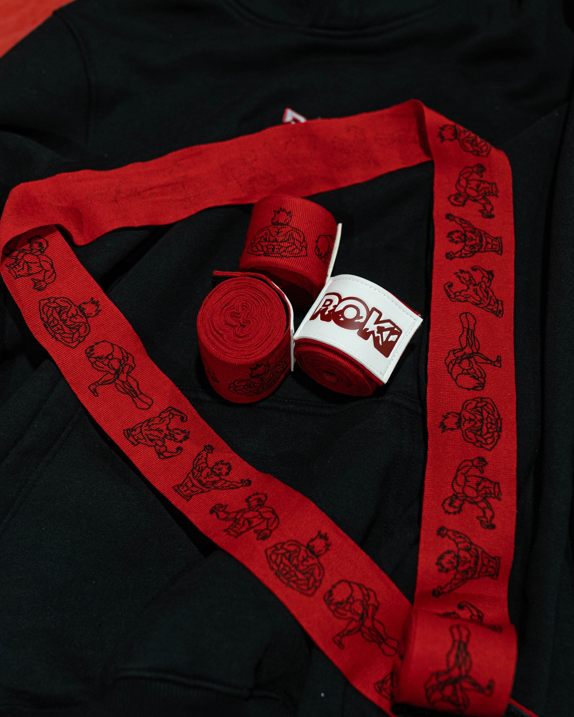 baki inspired red boxing hand wraps with anime grappler print and roki patch, partially rolled out on black gym hoodie