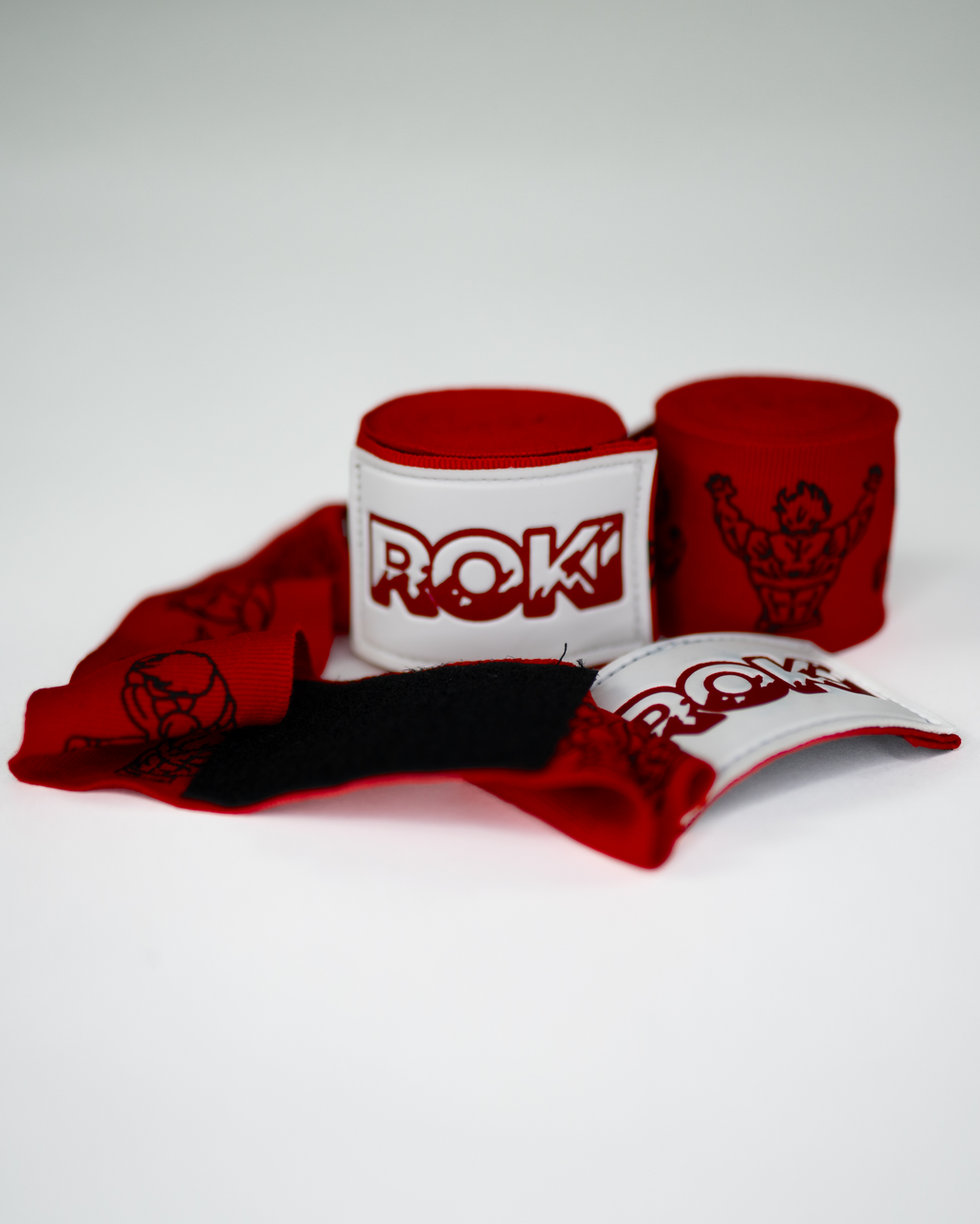 baki inspired red boxing hand wraps with anime grappler illustrations and bold roki patch, partially unrolled on white background
