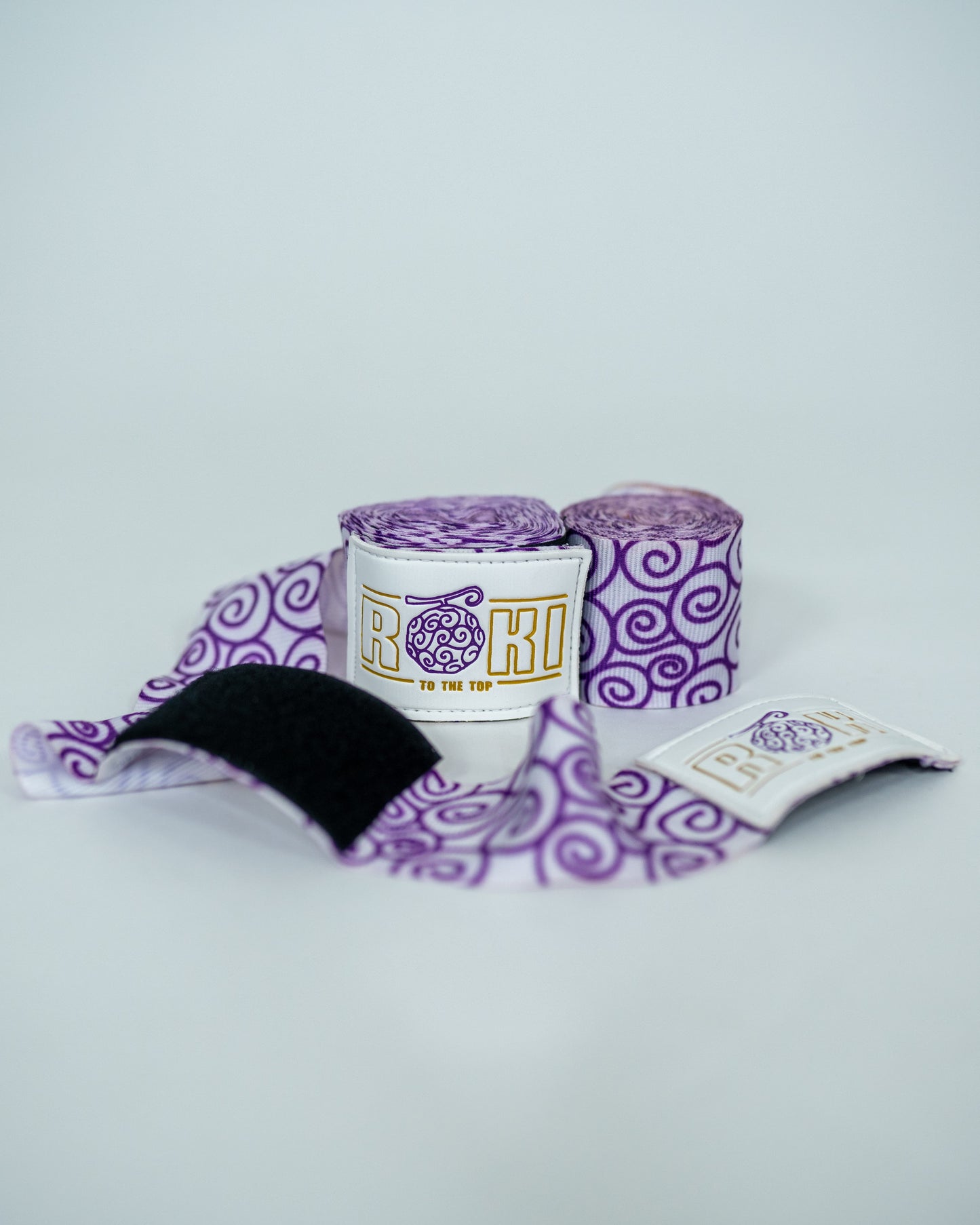 Roki gomu hand wraps rolled up, featuring purple accents, roki logo, thumb-loop and velcro patch
