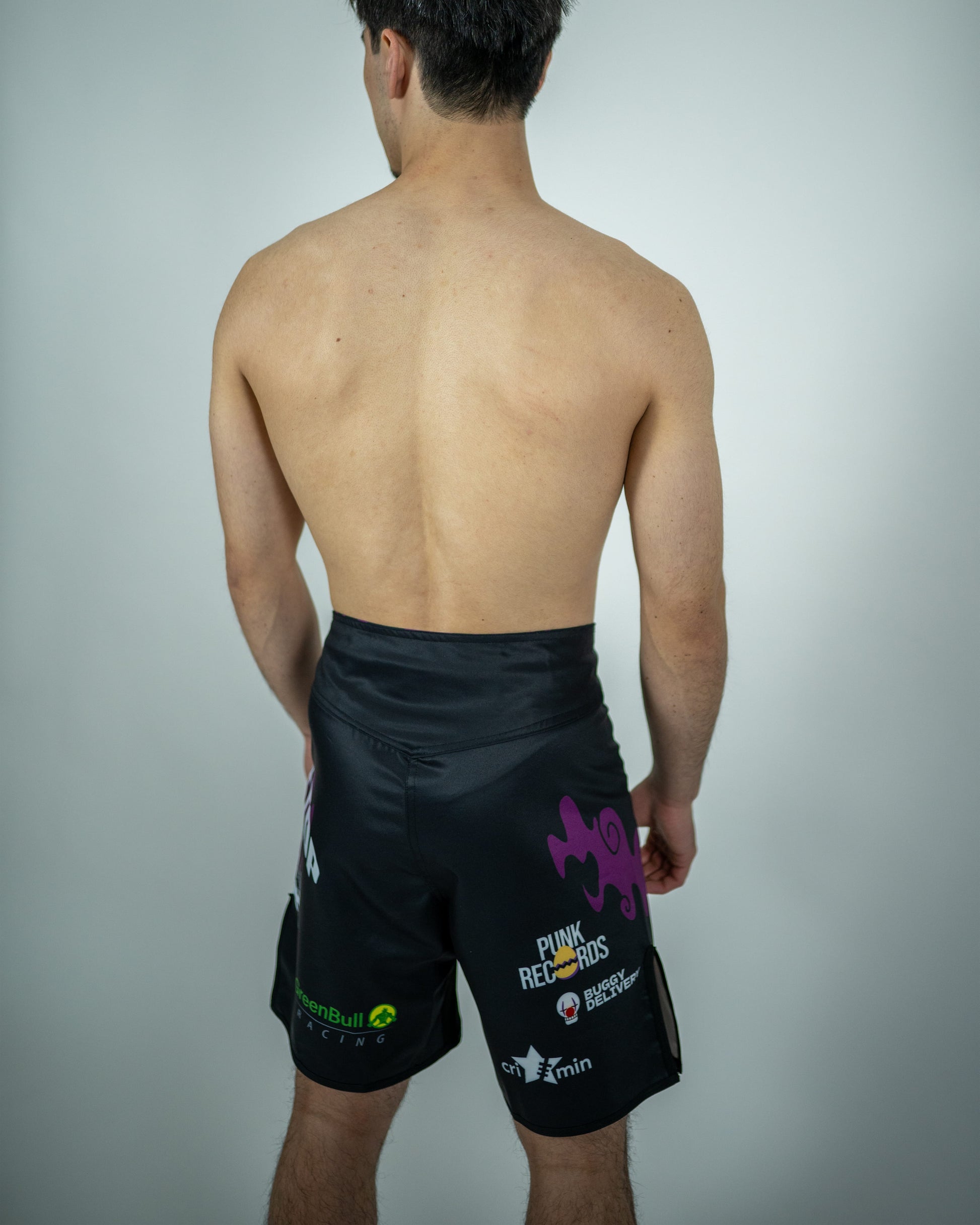 Back view of a model wearing Roki grand line fight shorts, featuring purple accents, Roki logo, and manga-inspired sponsor logos