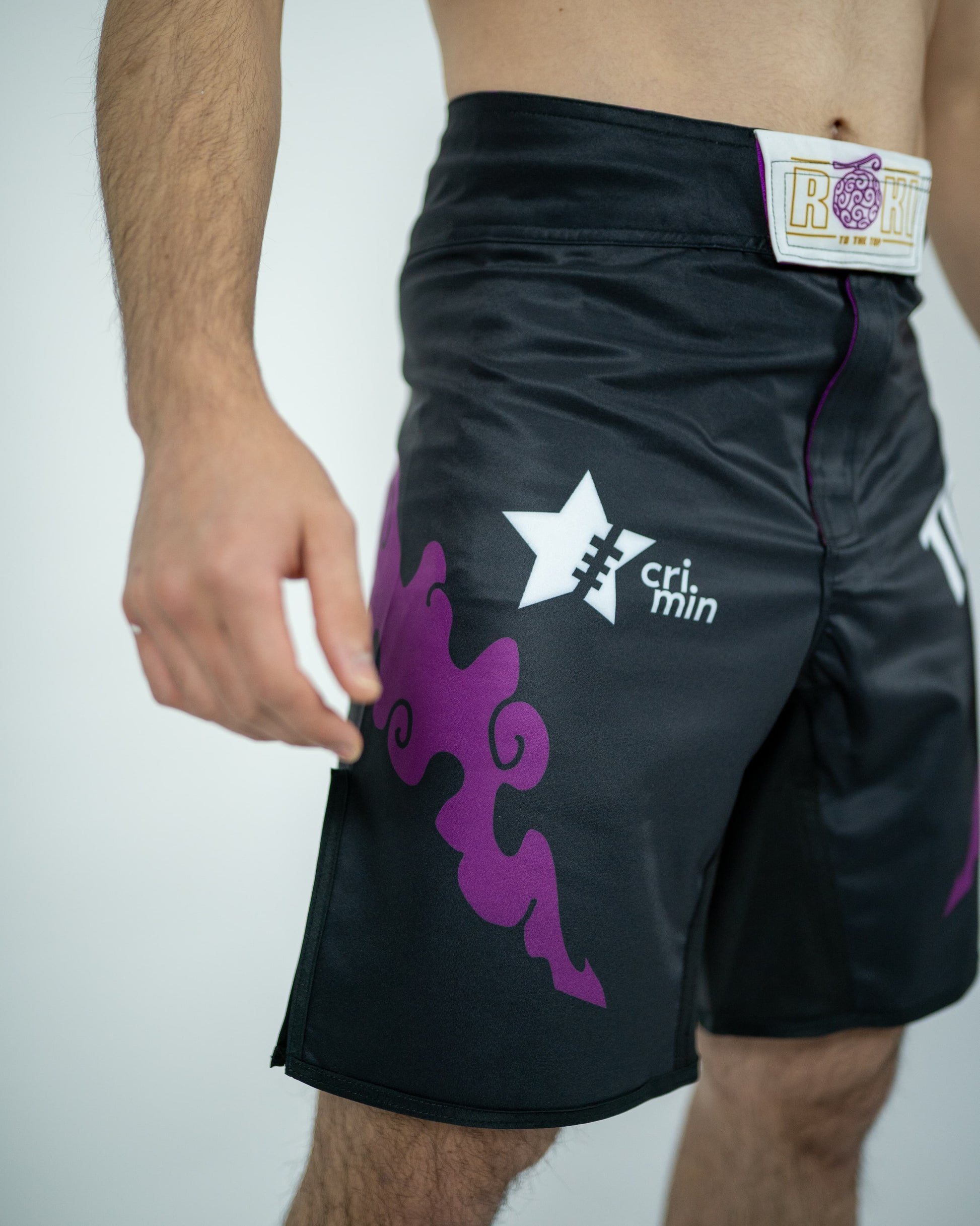 Side view of a model wearing Roki grand line fight shorts, featuring purple accents, Roki logo, and manga-inspired sponsor logos
