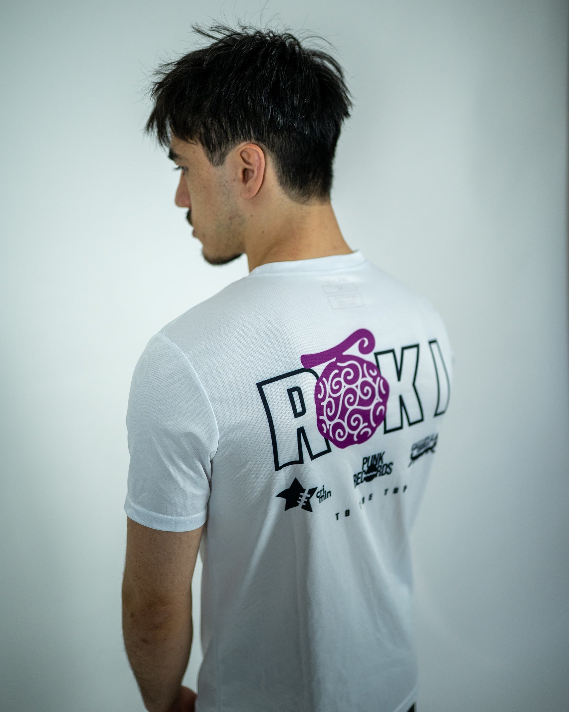 Over-shoulder view of a model wearing a white Roki Liberation training shirt with anime-inspired sponsor logos