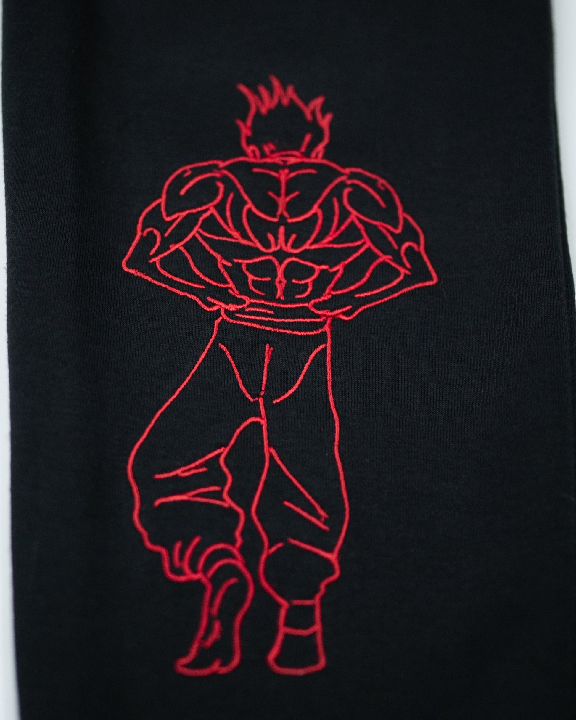 Close-up of Grappler Joggers lower leg showing red embroidery of back-facing demon back character on black fabric