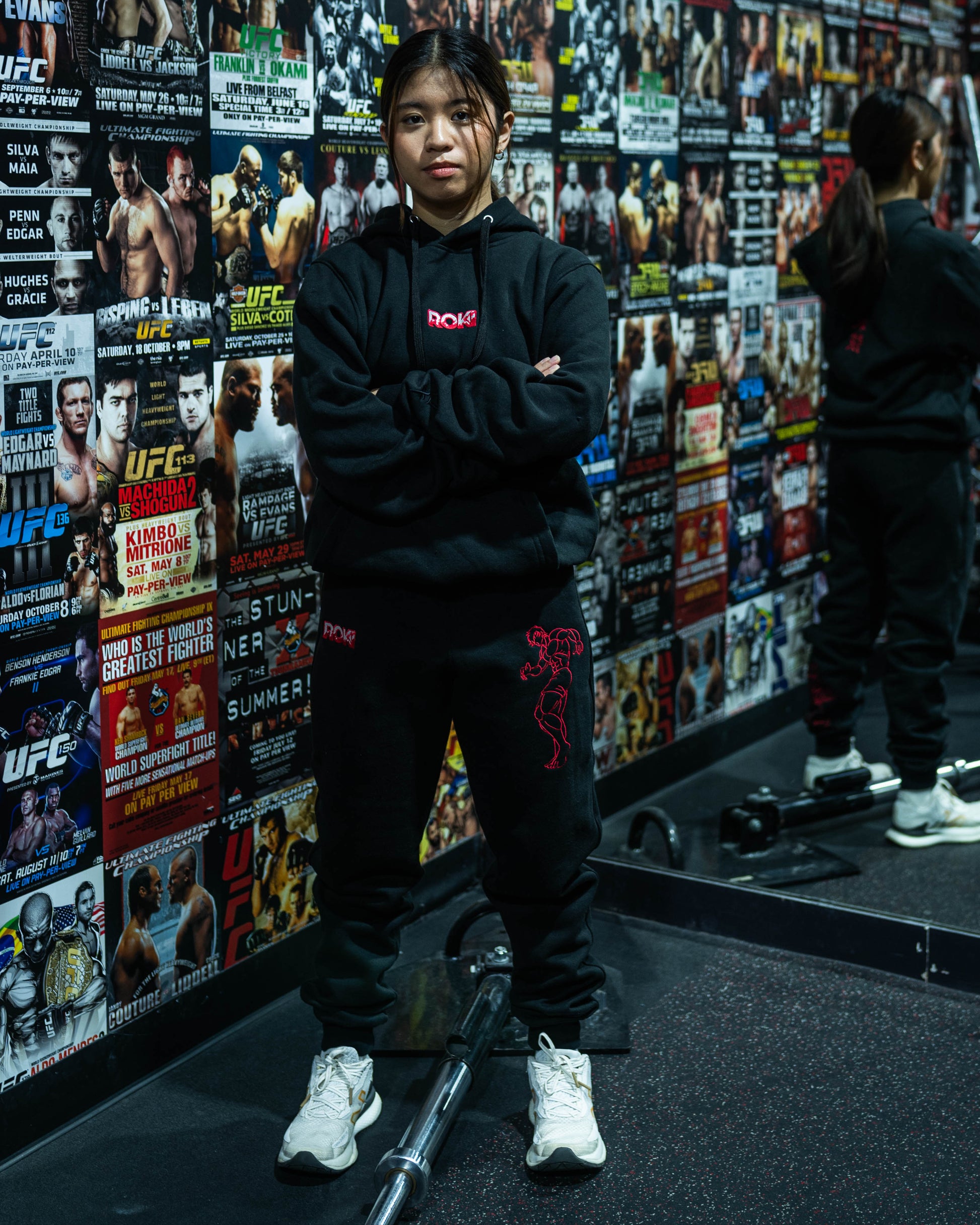 Model wearing Grappler Joggers and matching hoodie in UFC-themed gym with red ROKI logo and demon back embroidery