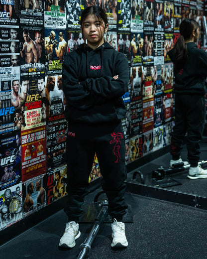 Model wearing Grappler Joggers and matching hoodie in UFC-themed gym with red ROKI logo and demon back embroidery