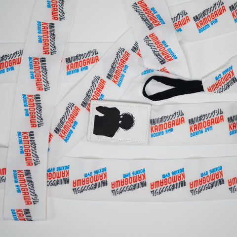 Flat lay of anime boxing hand wraps with Kamogawa Boxing Gym print and Ippo patch, showing thumb loop and repeating logo design
