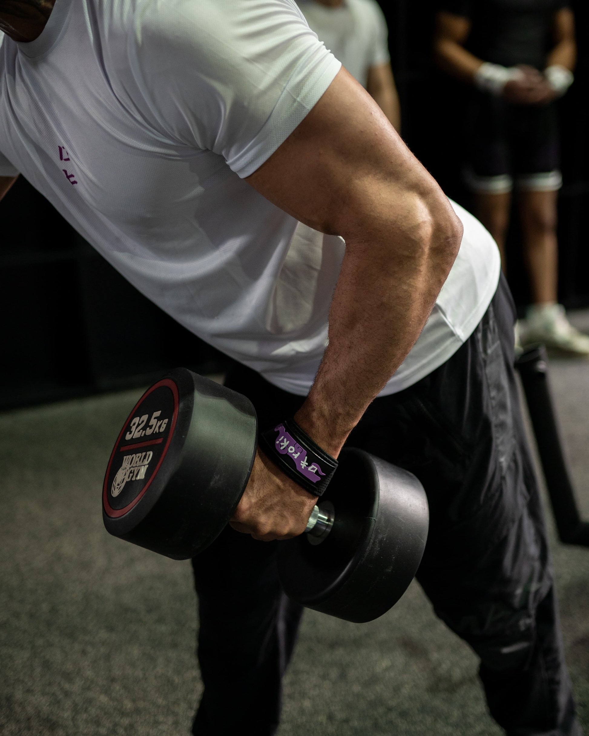 Close-up of a model wearing black Roki fruit lifting straps, lifting a dumbbell in a gym