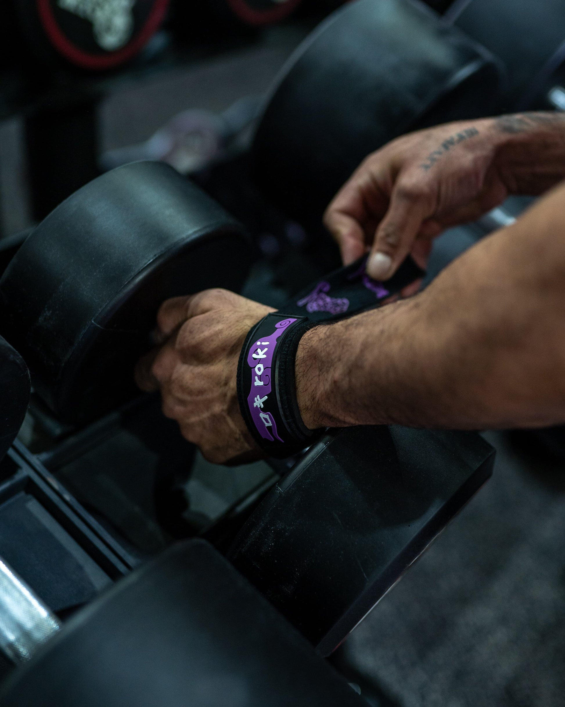 Close-up of a model wearing black Roki fruit lifting straps, lifting a dumbbell in a gym