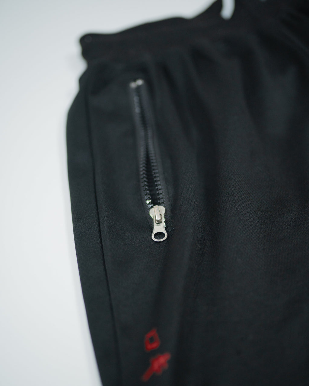 Detailed view of zippered pocket on Roki Gym Shorts with subtle red logo print on black fabri