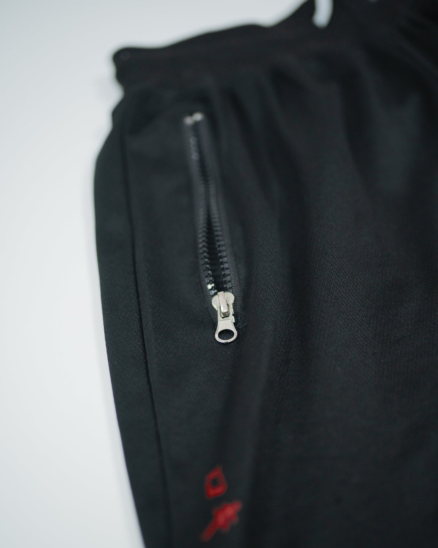 Detailed view of zippered pocket on Roki Gym Shorts with subtle red logo print on black fabri