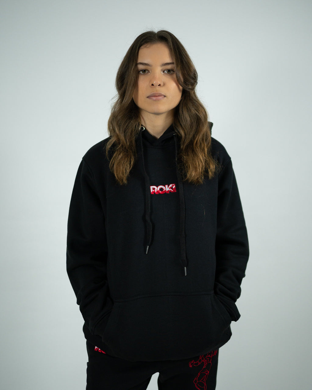 Female model wearing Sekai Saikyo Hoodie with red ROKI logo and relaxed pump-cover fit paired with demon back sweatpants