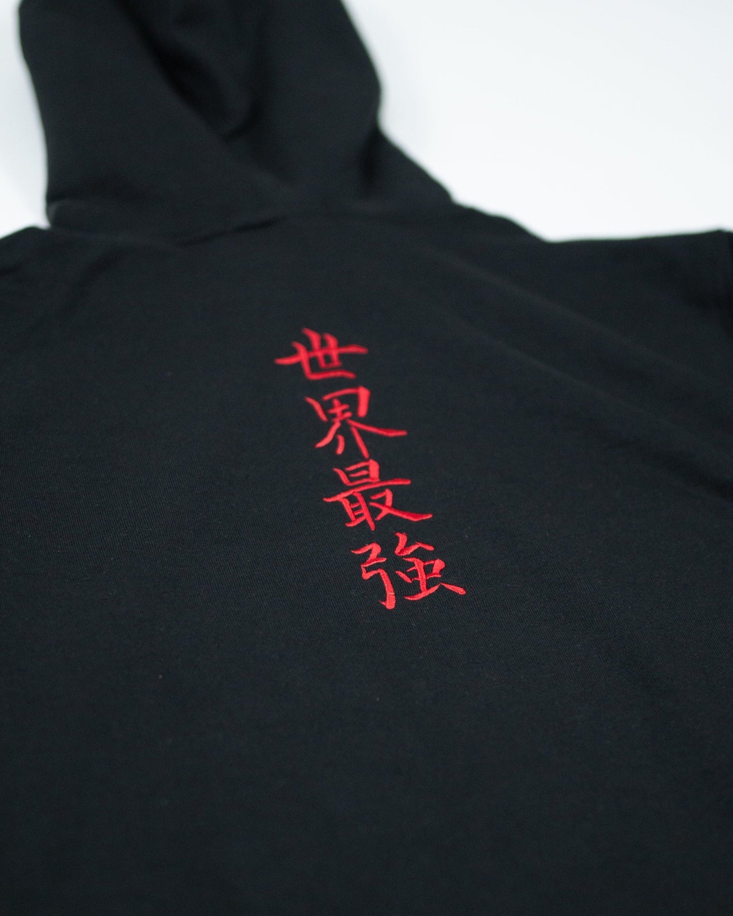Close-up of Sekai Saikyo Hoodie showing red embroidered kanji reading world's strongest on black fabric