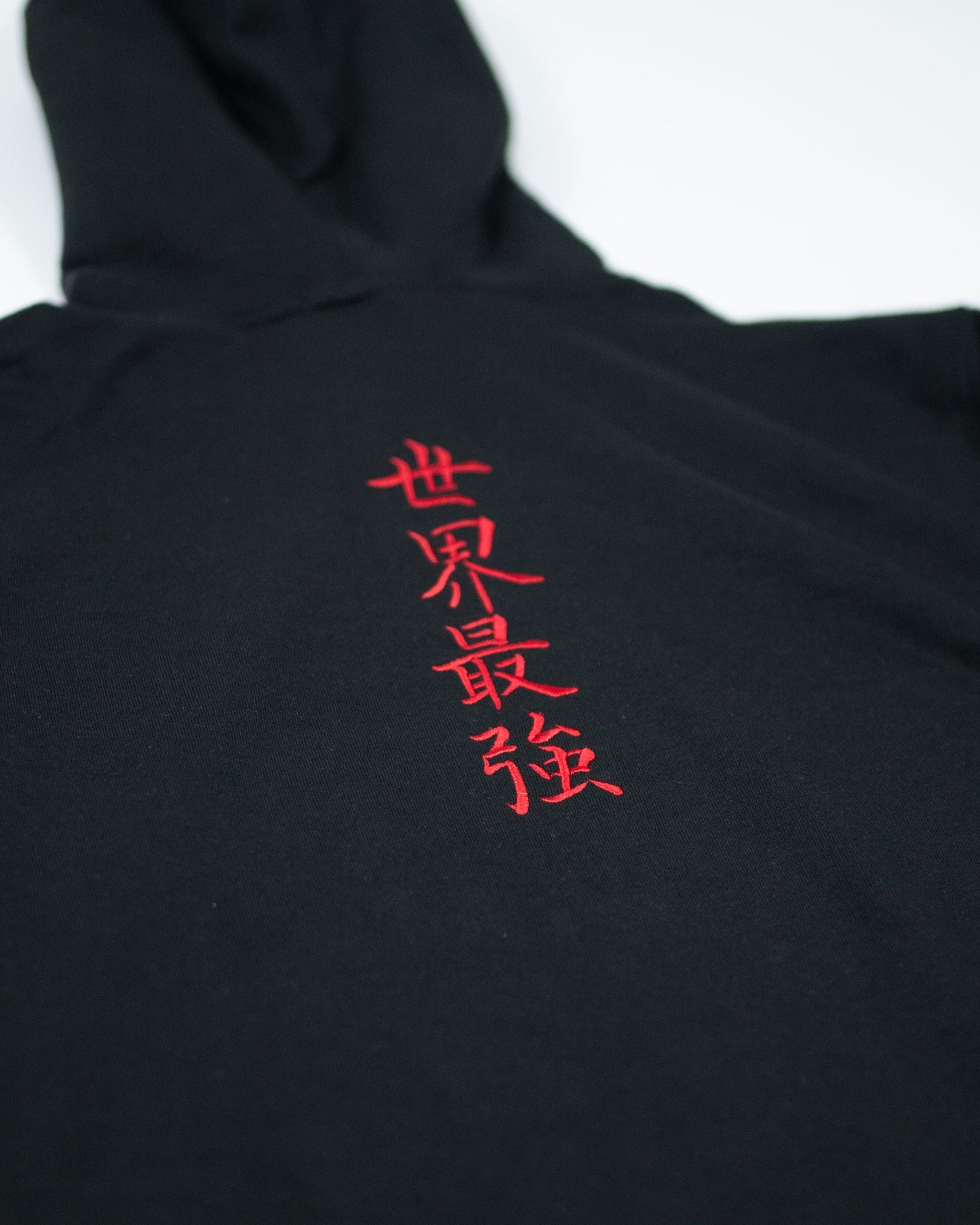Close-up of Sekai Saikyo Hoodie showing red embroidered kanji reading world's strongest on black fabric